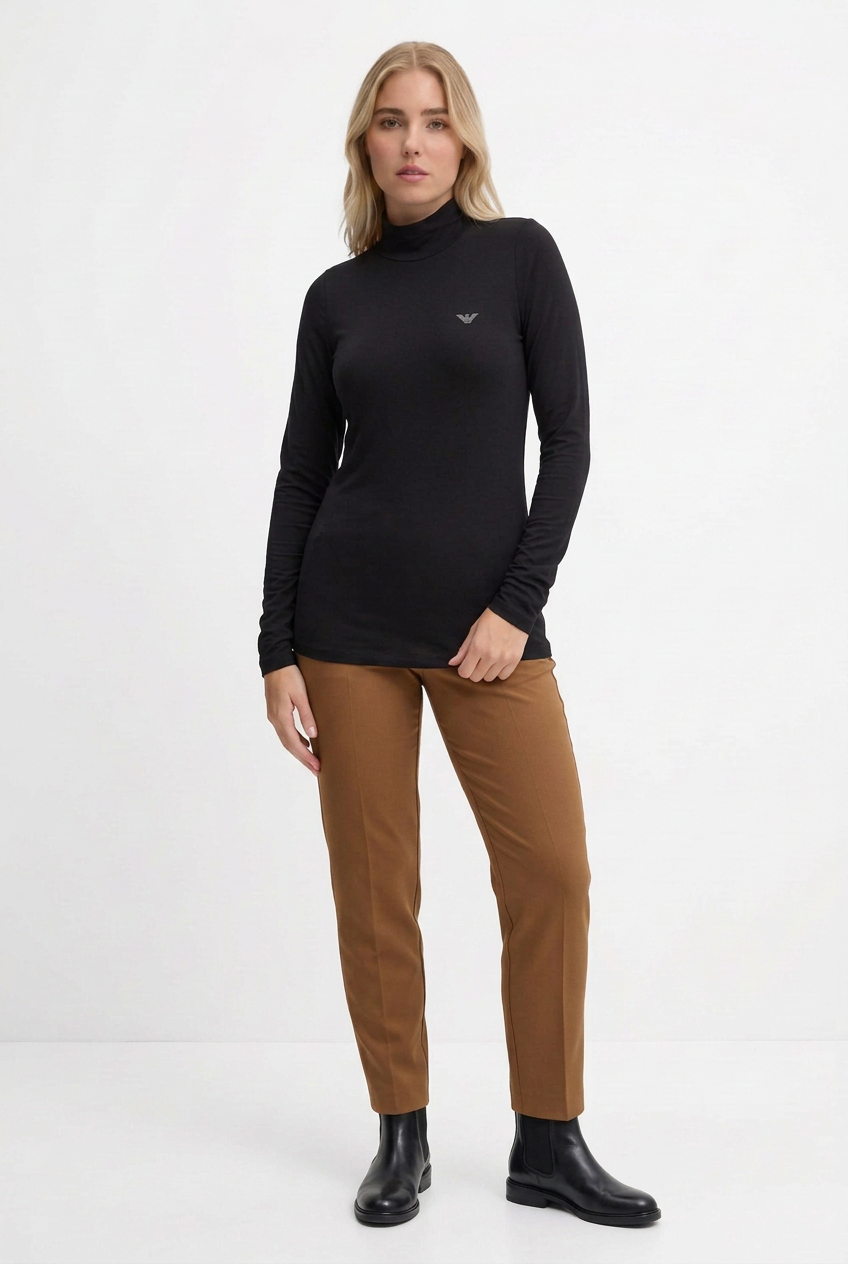 Modella con maglia nera con logo, pantaloni nocciola e stivaletti Beatles neri su sfondo bianco