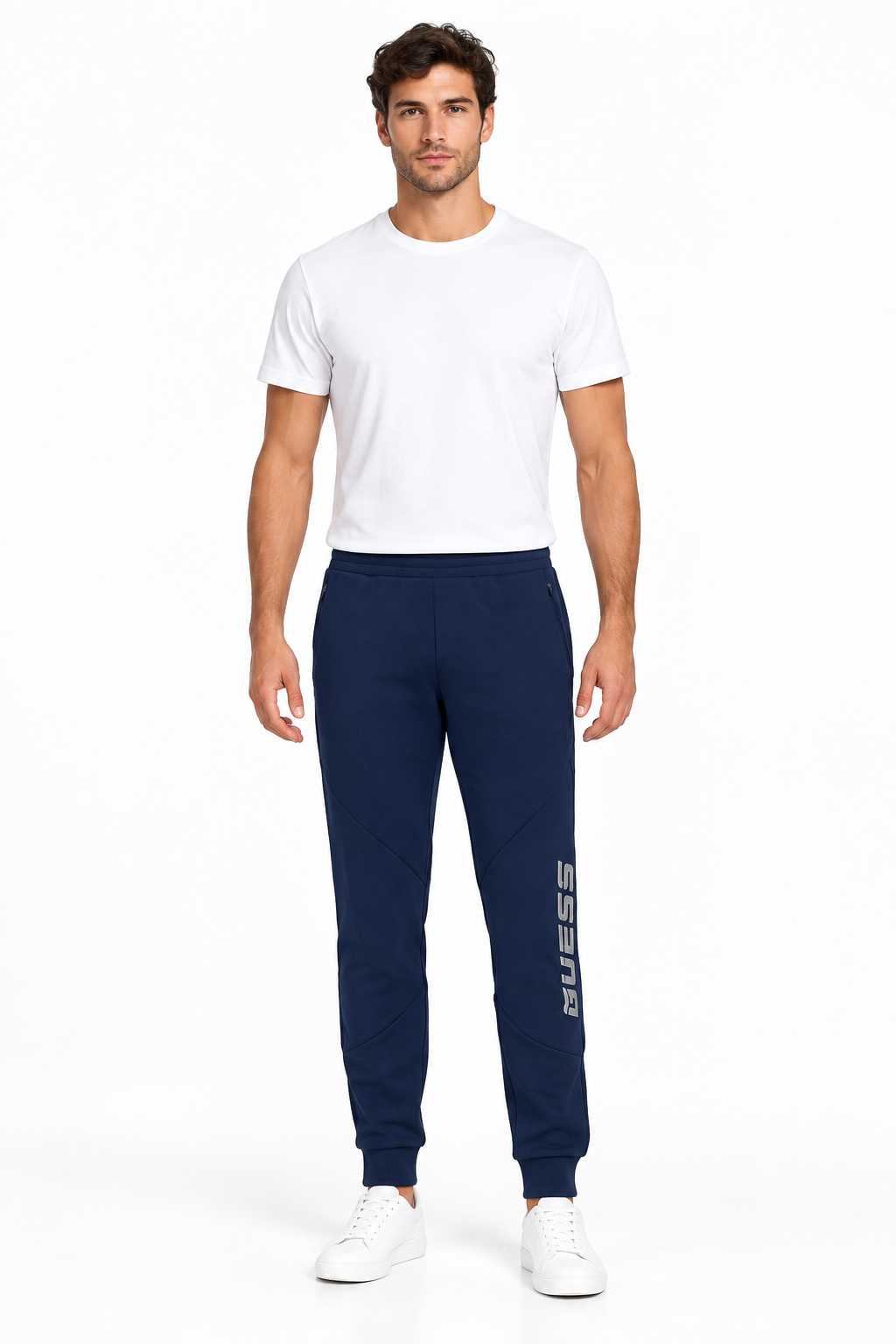 Modello a figura intera con pantaloni Guess navy e sneakers bianche su sfondo bianco