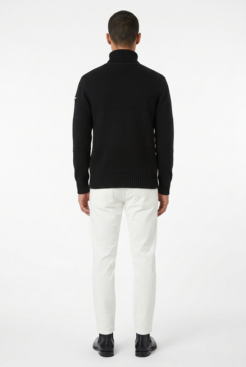 Modello visto da dietro con dolcevita Schott nero, pantaloni bianchi in velluto millerighe e stivaletti Beatles neri