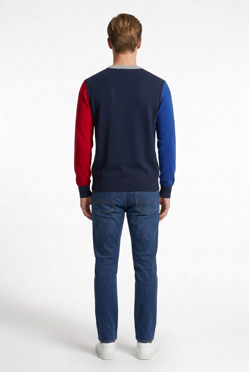 Modello visto da dietro con maglione color block, jeans indaco e sneakers bianche