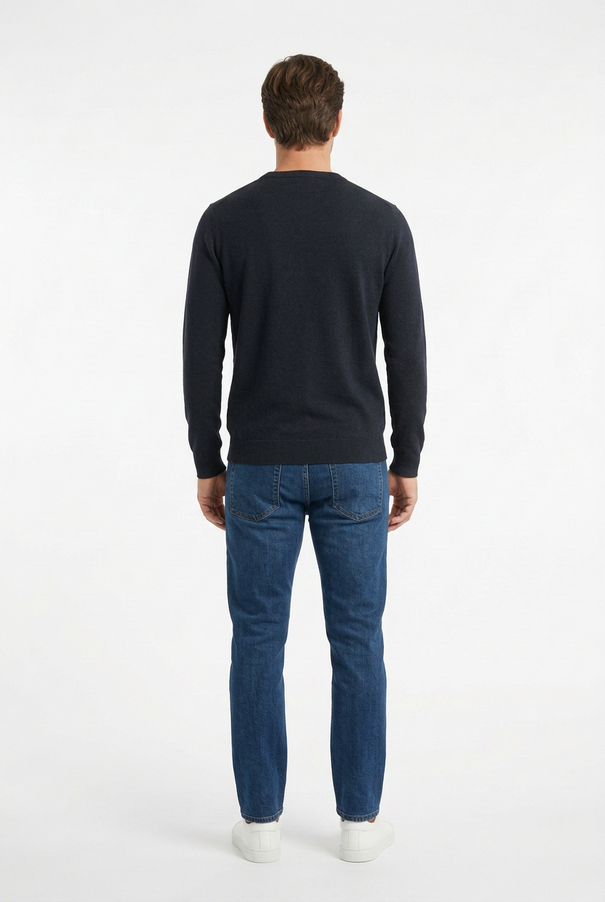 Modello visto da dietro con maglione navy, jeans indaco e sneakers bianche su sfondo bianco